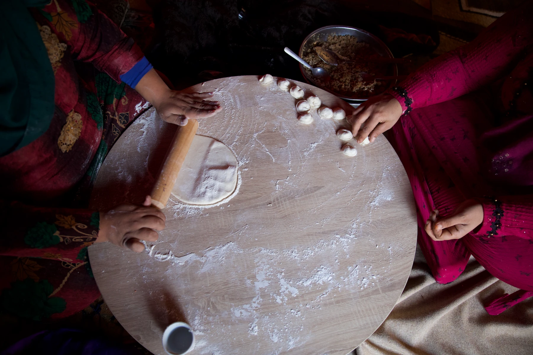 Two pairs of hands rolling and shaping dough on a round table.